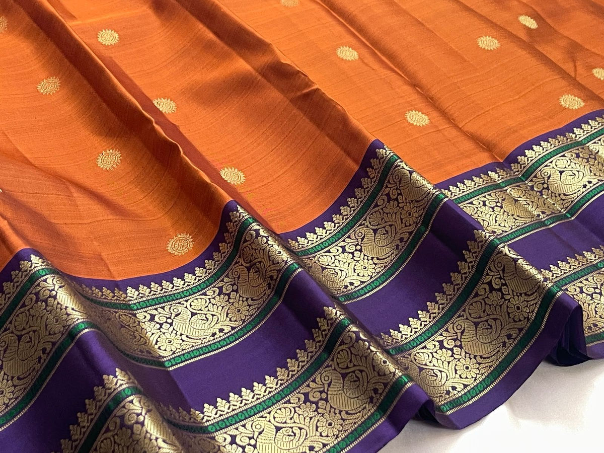 Orange silk body showing small sunburst-style gold zari buttas placed with open spacing across the saree field.