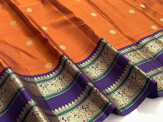 Orange silk body showing small sunburst-style gold zari buttas placed with open spacing across the saree field.