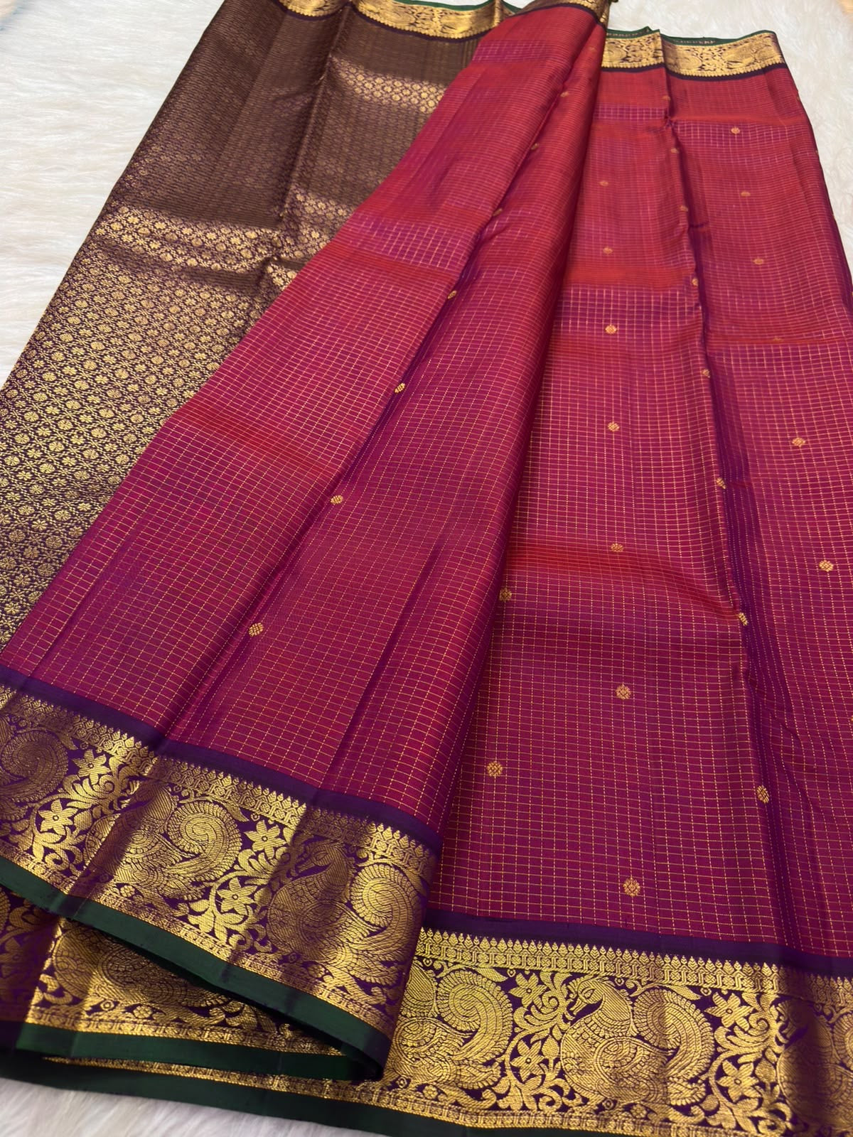 Broad aubergine-purple border with antique-gold peacock and malar kodi vine zari and forest-green edge on raspberry red Kanchipuram silk saree