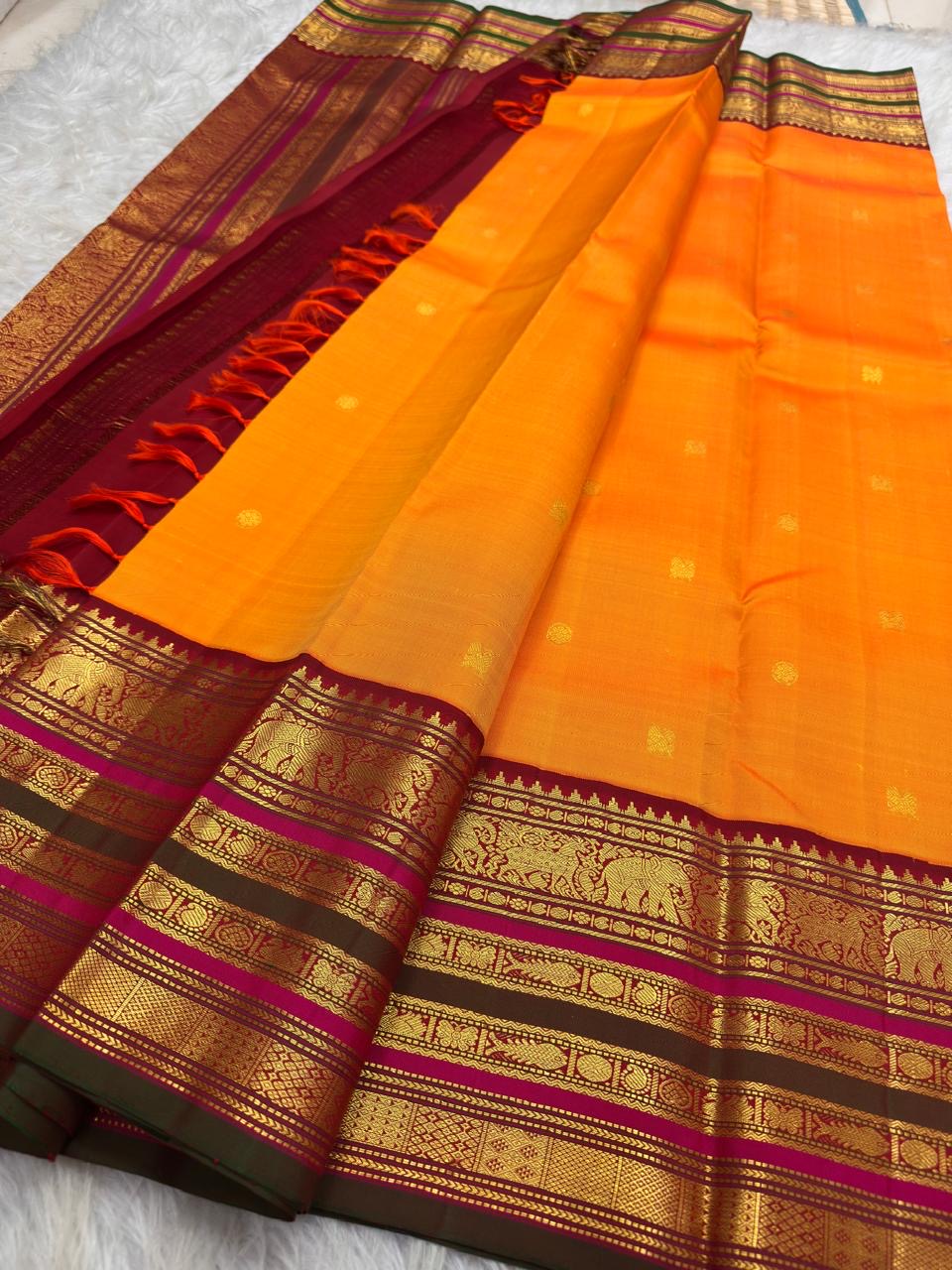 Bright marigold orange Kanchipuram silk saree with gold buttas and deep red ornate Varisaipet border.
