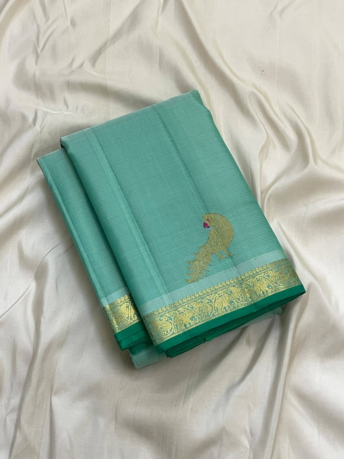Folded aqua green Kanchipuram silk saree showing handwoven gold zari mayil butta and floral zari border