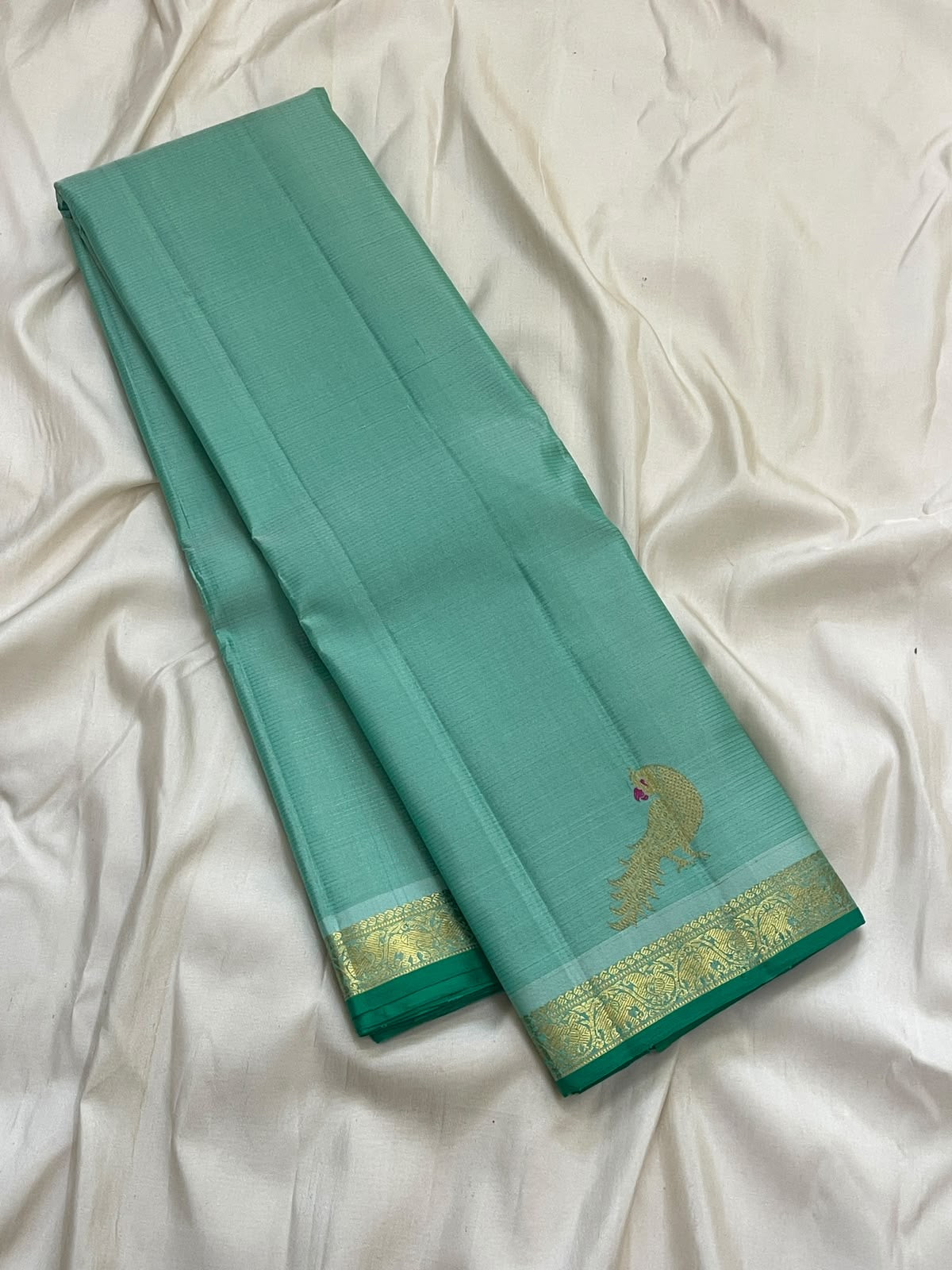 Folded seafoam blue green Vairaoosi silk saree with deep green selvedge and narrow ornamental gold border