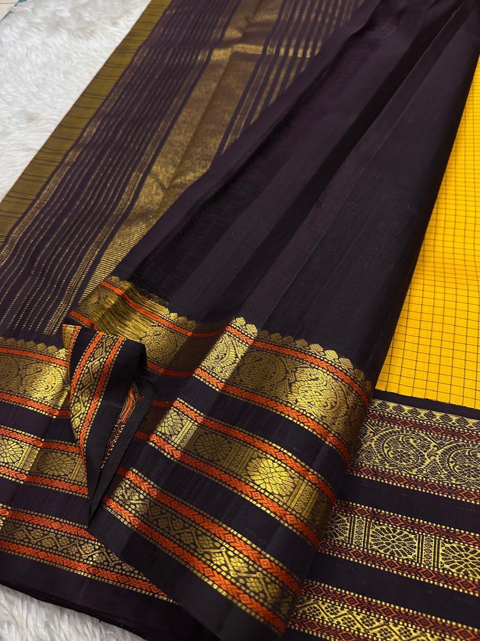 Folded mustard checked Kanchipuram silk saree with deep navy and antique gold zari border, placed on a woven mat.