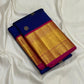 Folded blue Kanchipuram silk saree with wide gold zari woven border and pink edge on white fabric backdrop.