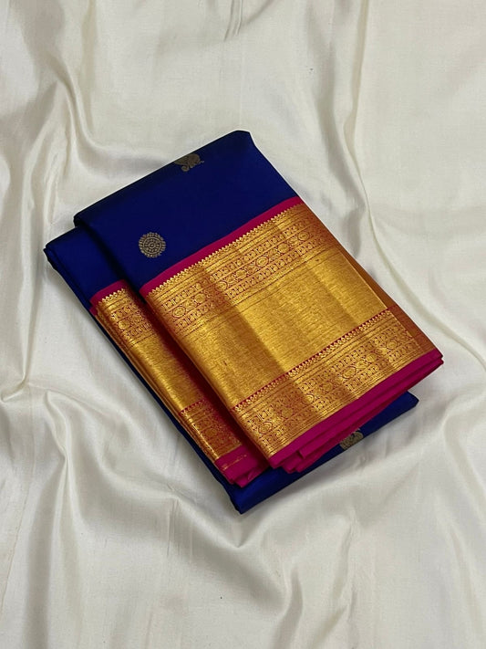 Folded blue Kanchipuram silk saree with wide gold zari woven border and pink edge on white fabric backdrop.