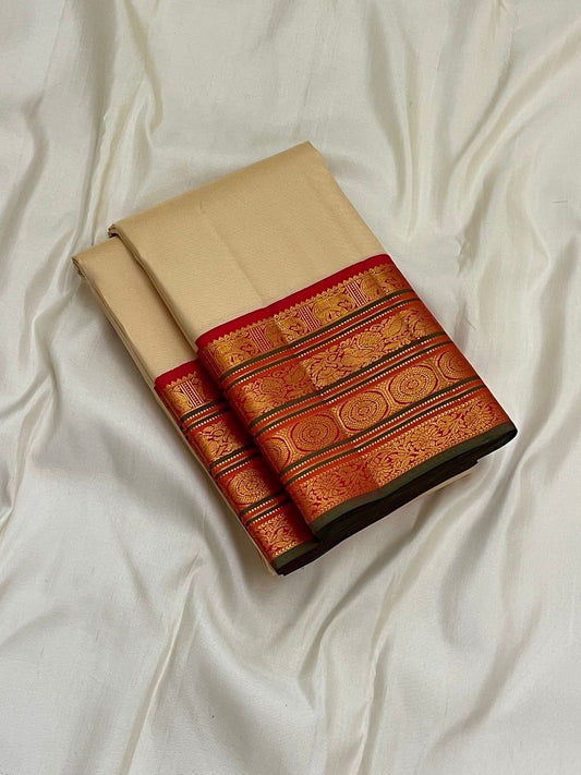 Folded pure Kanchipuram silk saree in ivory with red zari woven border, shown on white fabric background.