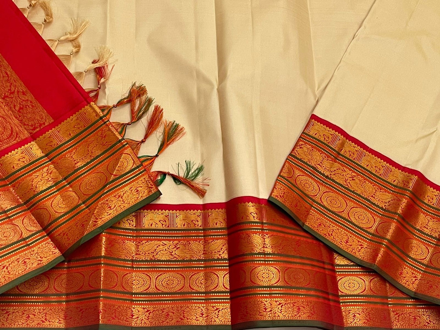 Draped border detail of an ivory pure Kanchipuram silk saree with red zari woven border and green edging.