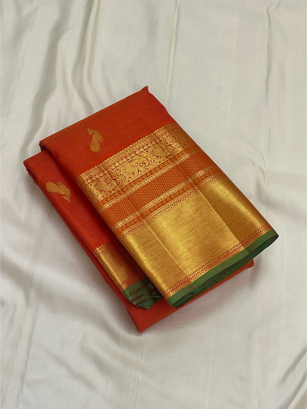 folded vermillion orange kanchipuram silk saree with gold zari border