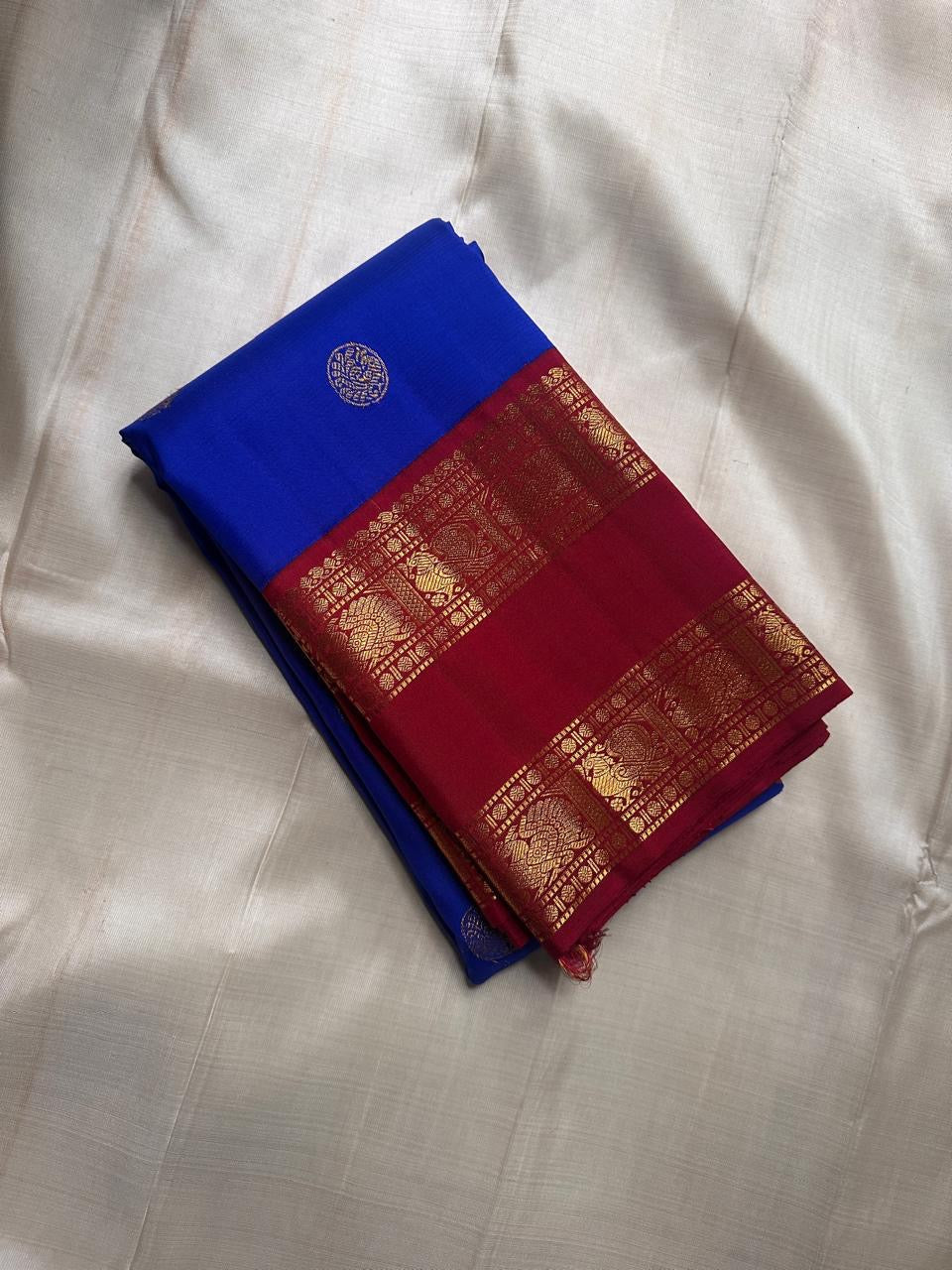 Folded Pure Kanchipuram silk saree in royal blue with a maroon zari woven border and a round silver motif on the fold.