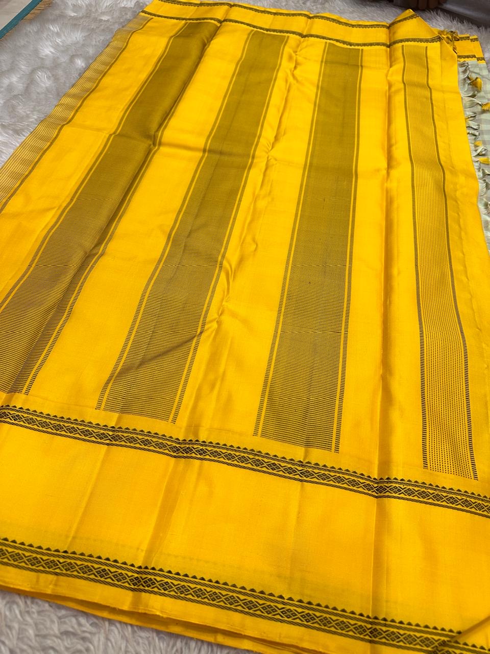 Stack of folded silk sarees on white cloth, including a sage checked and mustard bordered Kanchipuram silk saree