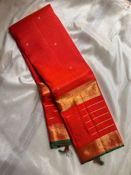 Folded vermilion orange pure Kanchipuram silk saree with gold zari border and green edge on ivory fabric