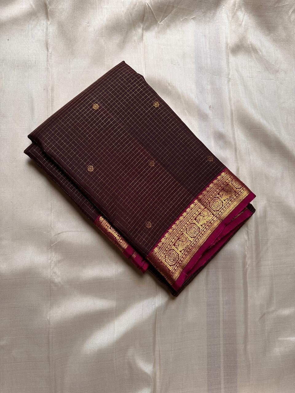 Folded deep brown checked pure Kanchipuram silk saree with magenta zari border on beige backdrop