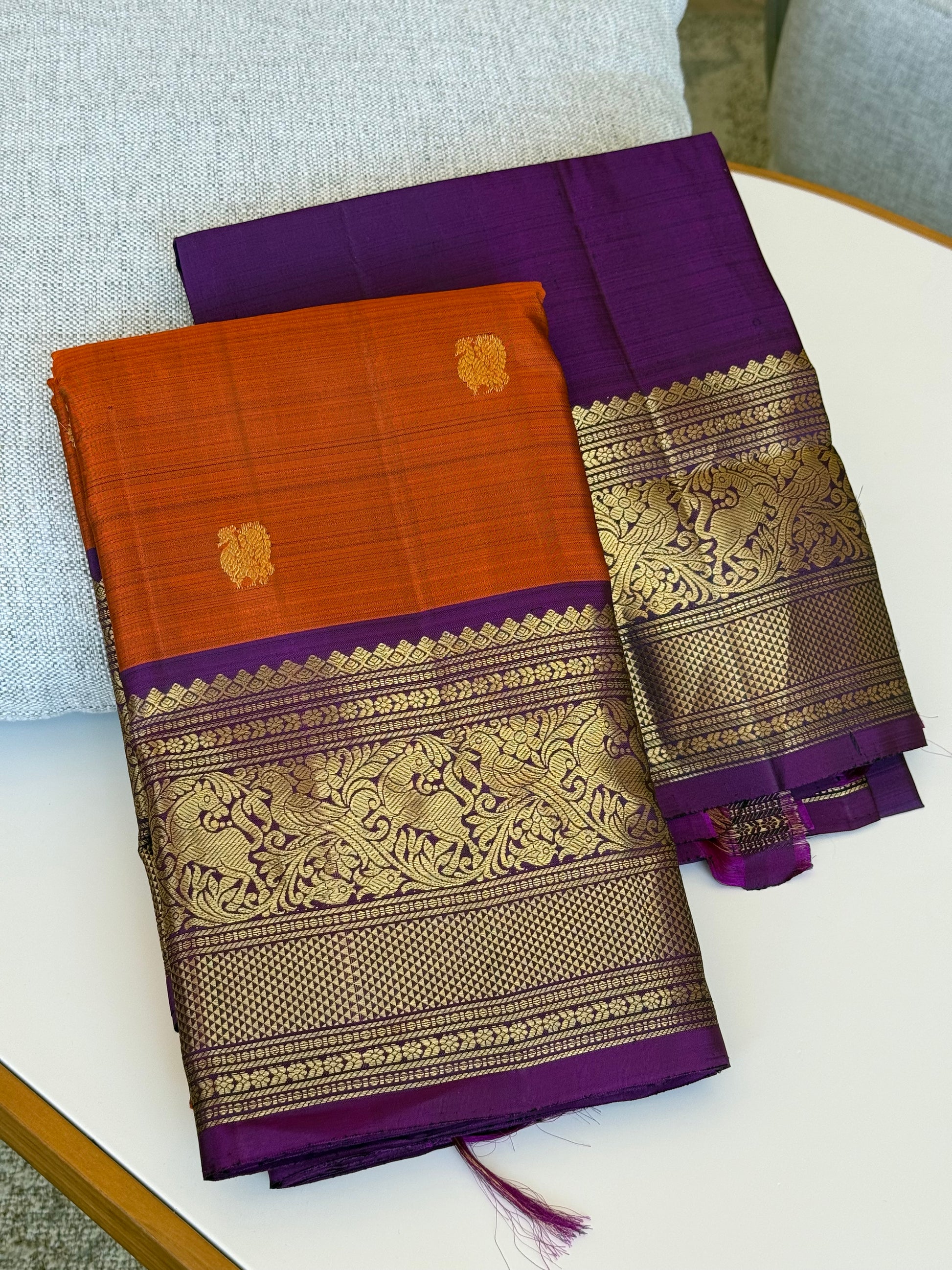 Folded view of rust orange purple Kanchipuram silk saree with intricate vanasringaram animal motifs