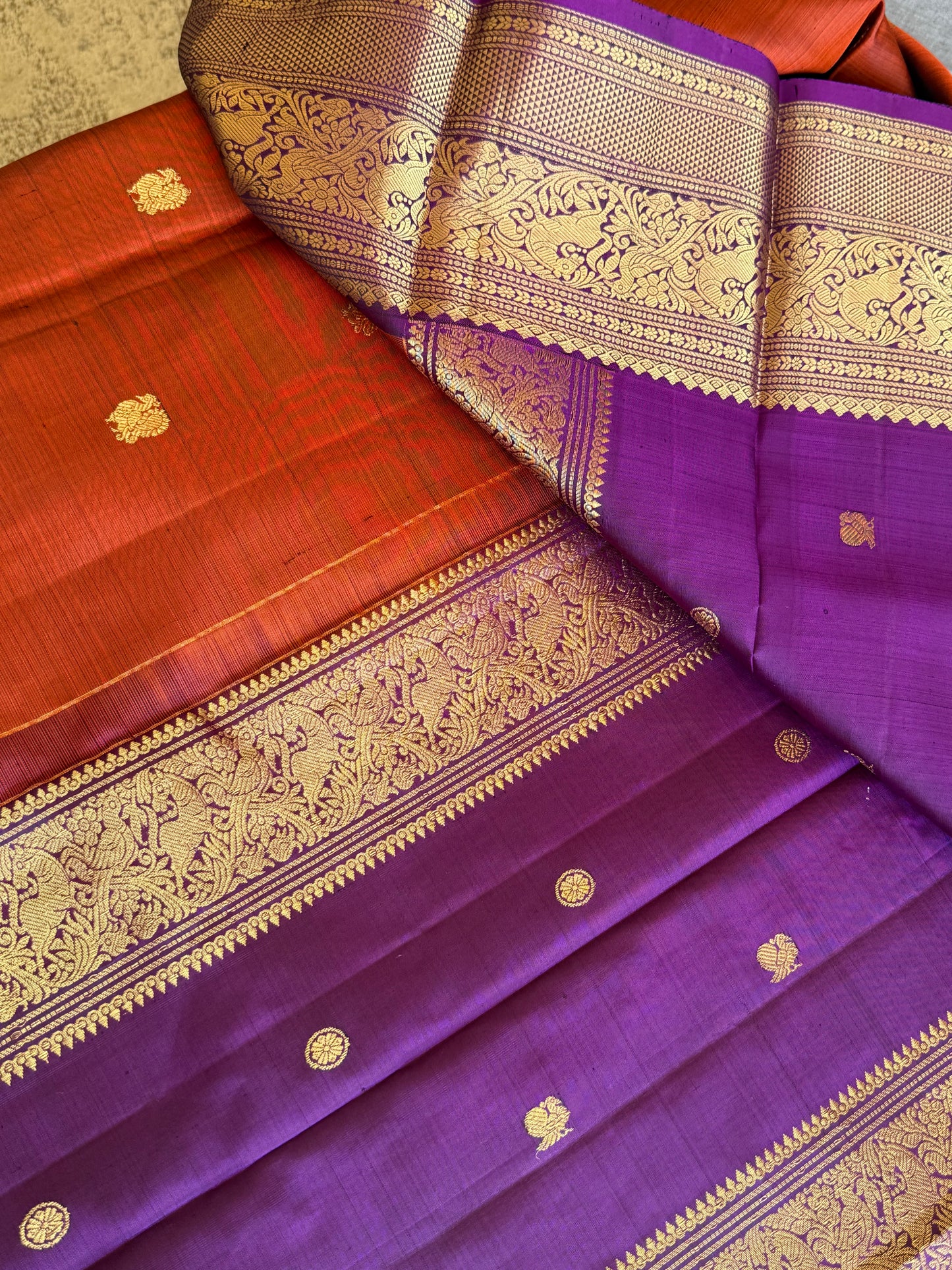 Folded view of rust orange purple Kanchipuram silk saree with intricate vanasringaram animal motifs