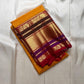 Folded Pure Kanchipuram Silk Saree in mustard yellow with wide gold zari border and maroon bands on ivory backdrop.