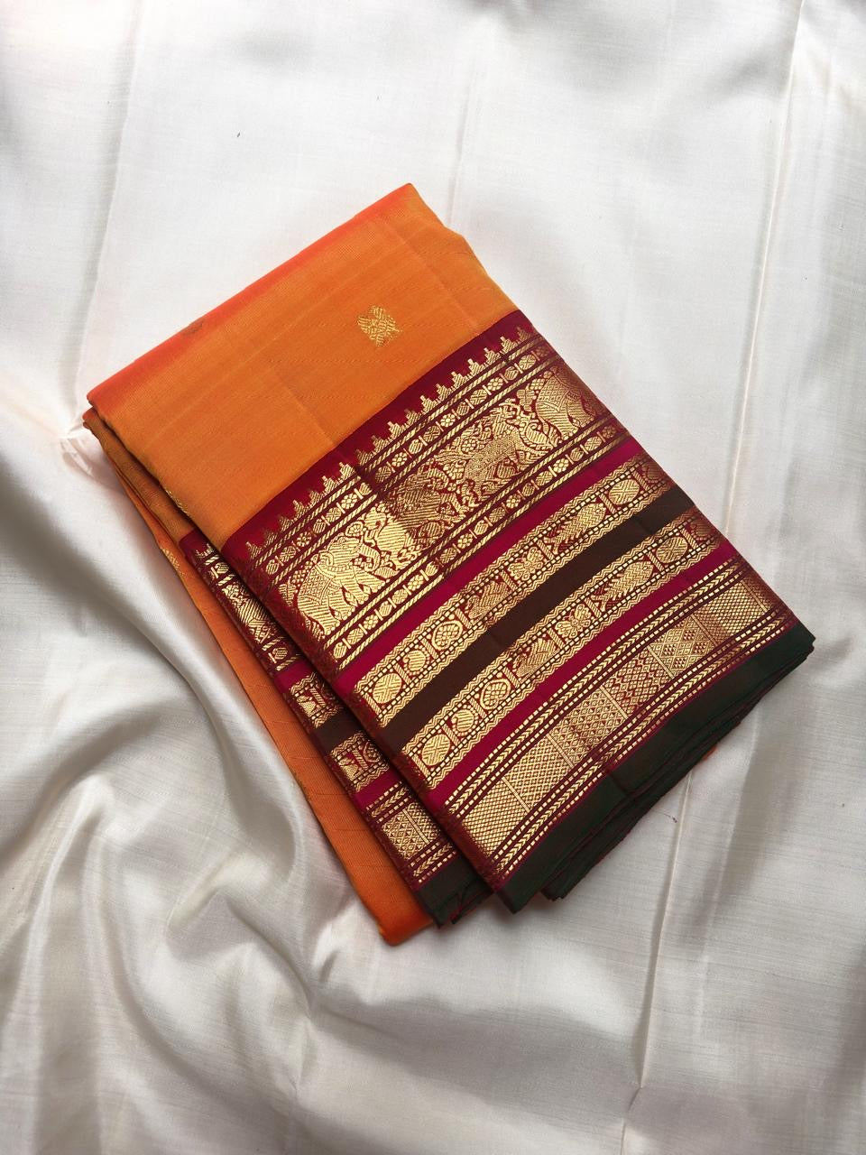 Grand red and antique gold zari pallu with ornamental bands and orange tassels.
