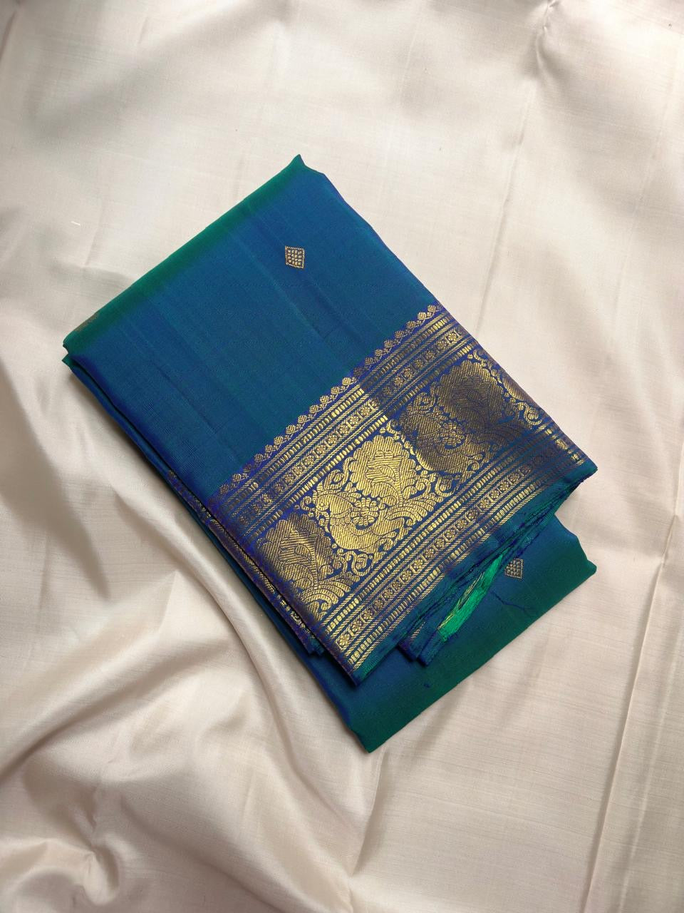 Peacock Blue, emerald green, royal blue and antique gold handwoven Kanchipuram butta silk saree, folded front, with gold zari detailing.