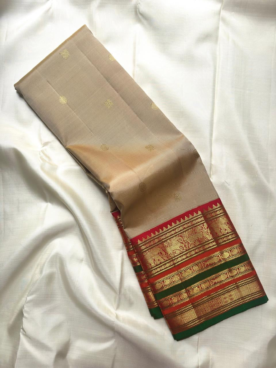 Sandalwood ivory Kanchipuram saree with gold buttas and Arakku red green ornate zari border.
