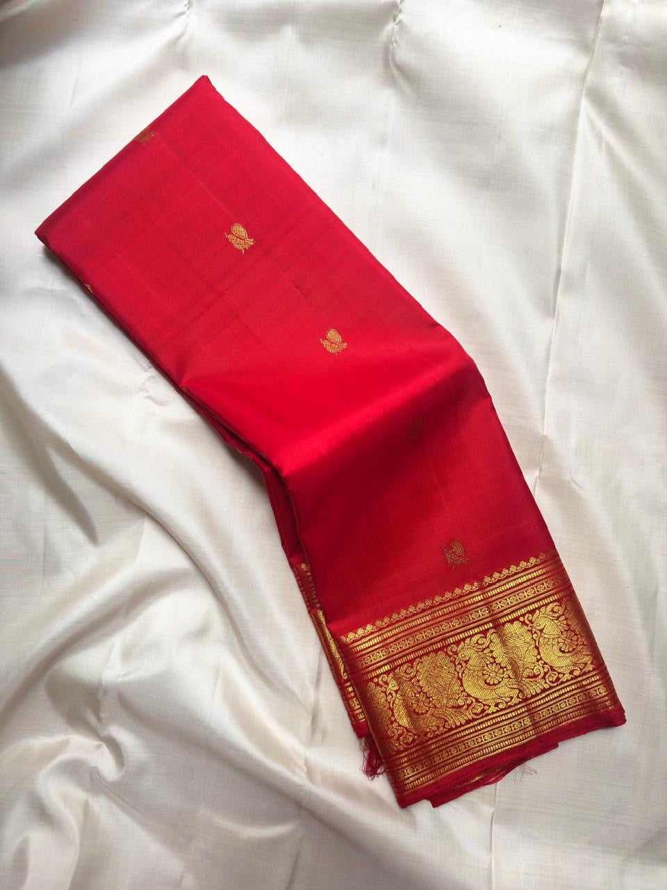 Vermilion red, warm Arakku-red undertones and rich yellow gold handwoven Kanchipuram butta silk saree, folded front, with gold zari detailing.