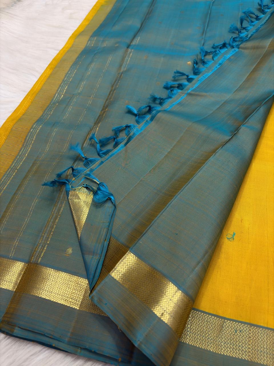 Turmeric yellow Kanchipuram silk saree opened to show peacock blue striped zari pallu and narrow border