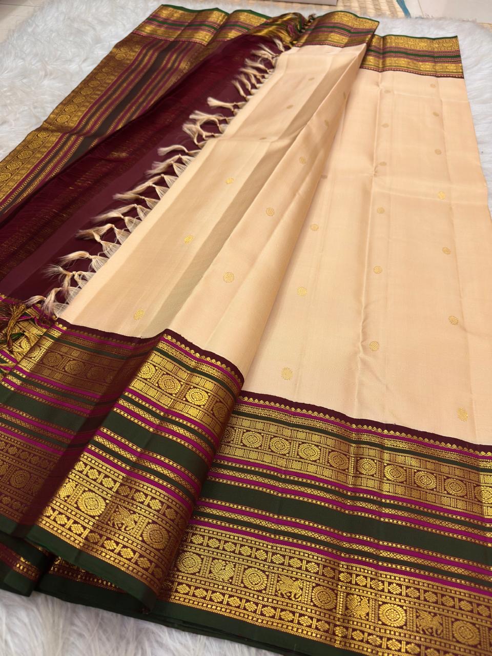 Soft peach ivory Kanchi Pattu silk saree with maroon and forest green border detail.