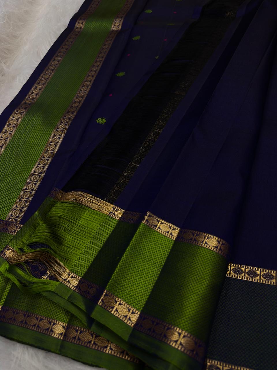 Deep midnight indigo Kanchipuram silk body with spaced green paisley-floral buttas and tiny magenta accents.