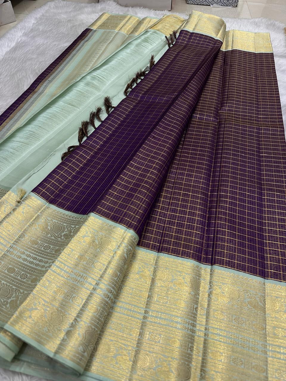 Deep aubergine-plum Kanchipuram silk body crossed with delicate fine classic-gold Zari Kattam lines.