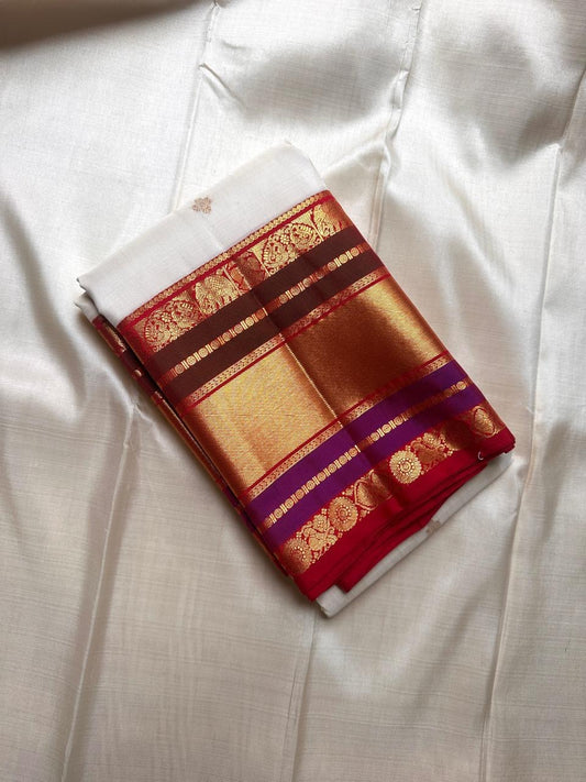 Folded Pure Kanchipuram silk saree in ivory with gold buttas and wide zari border with red, maroon, and purple bands.