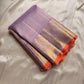 Folded lavender pure Kanchipuram silk saree with gold zari border and orange selvedge on beige silk backdrop.