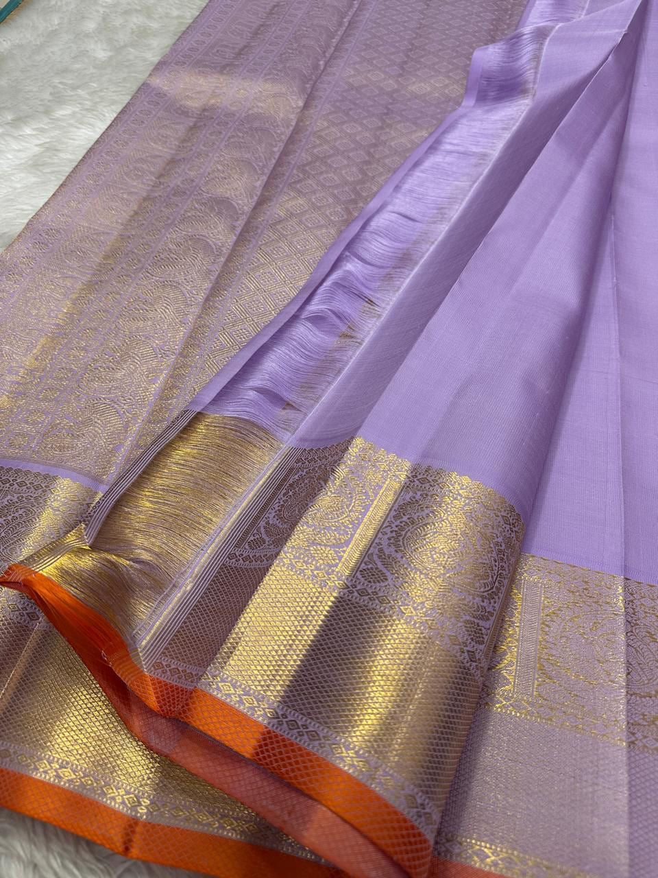 Close-up of lavender pure Kanchipuram silk saree showing gold zari border panels and orange selvedge.