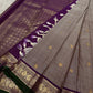 Grey pure Kanchipuram silk saree drape beside a purple pallu with heavy gold zari woven pattern and white-purple tassels.