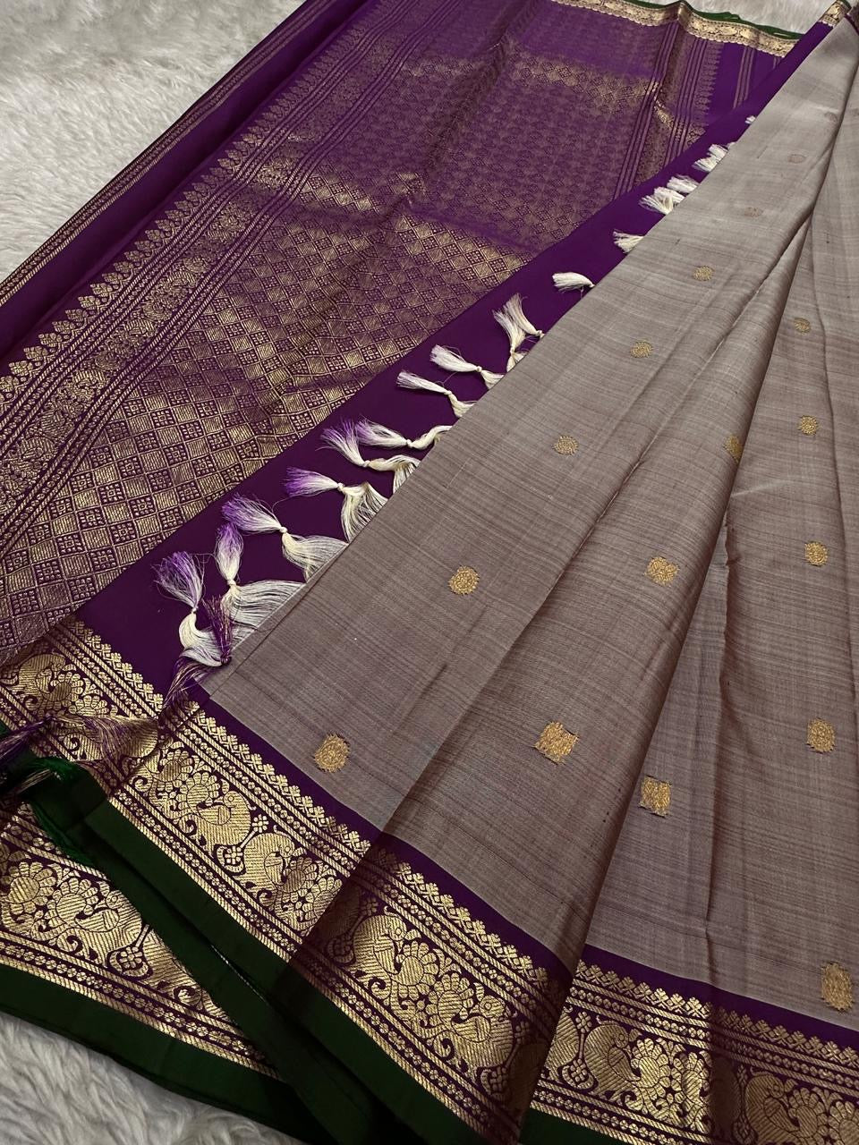 Grey pure Kanchipuram silk saree drape beside a purple pallu with heavy gold zari woven pattern and white-purple tassels.