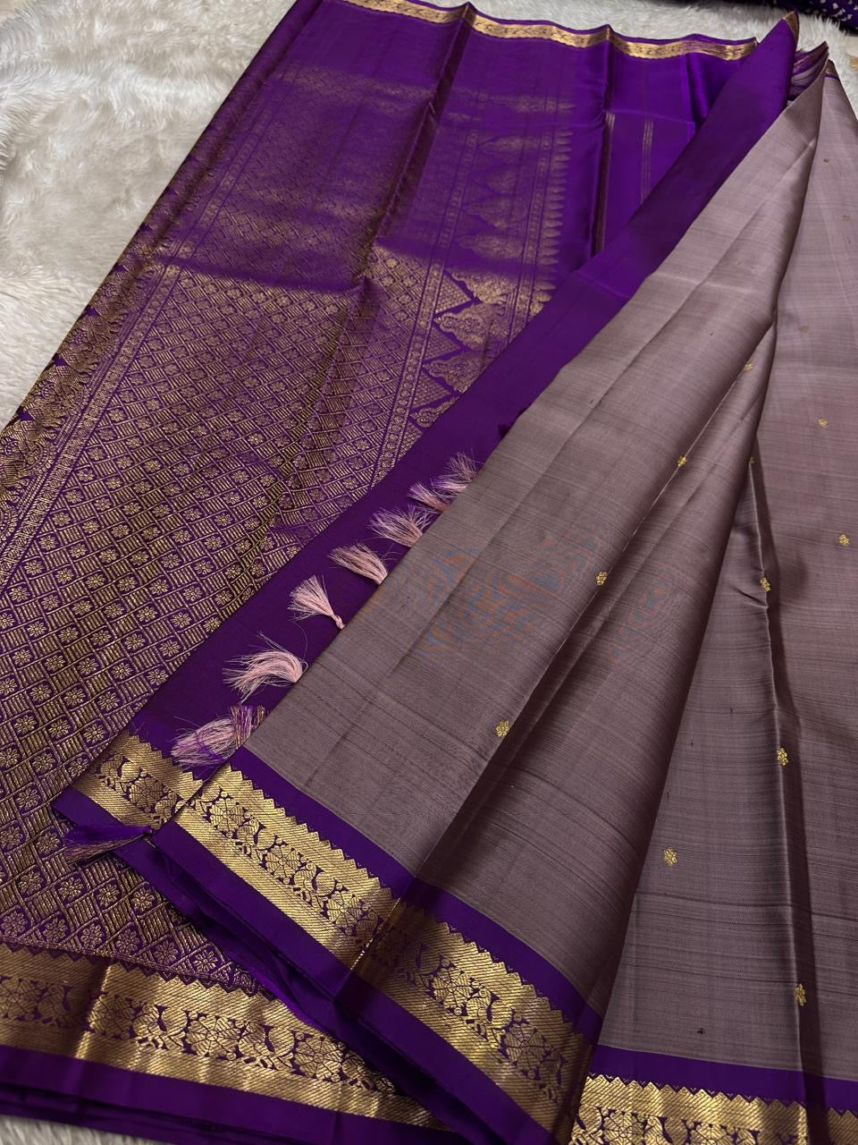 Close view of deep purple pallu with dense gold zari woven pattern and broad zari border along the edge.