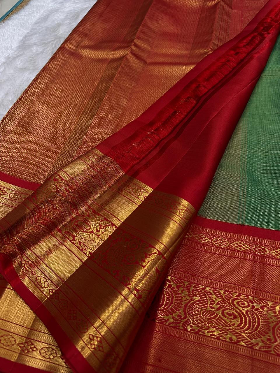 Handwoven pure silk tissue Kanchipuram saree in leaf green with small gold buttas and a kumkum red border.