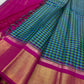 Folded checked Kanchipuram silk saree with magenta border and gold zari panel beside another folded saree on ivory backdrop