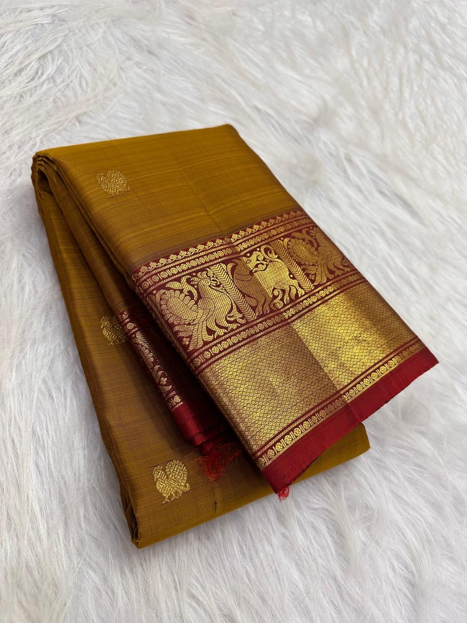 Folded Manjal gold pure silk Kanchipuram saree with spaced zari buttas and a deep Arakku Yazhi border.
