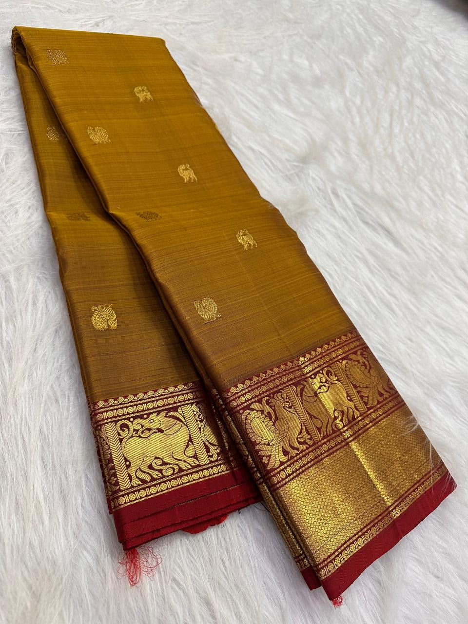 Burnished Manjal body showing open placement of figurative and floral thanga-zari buttas across the silk field.