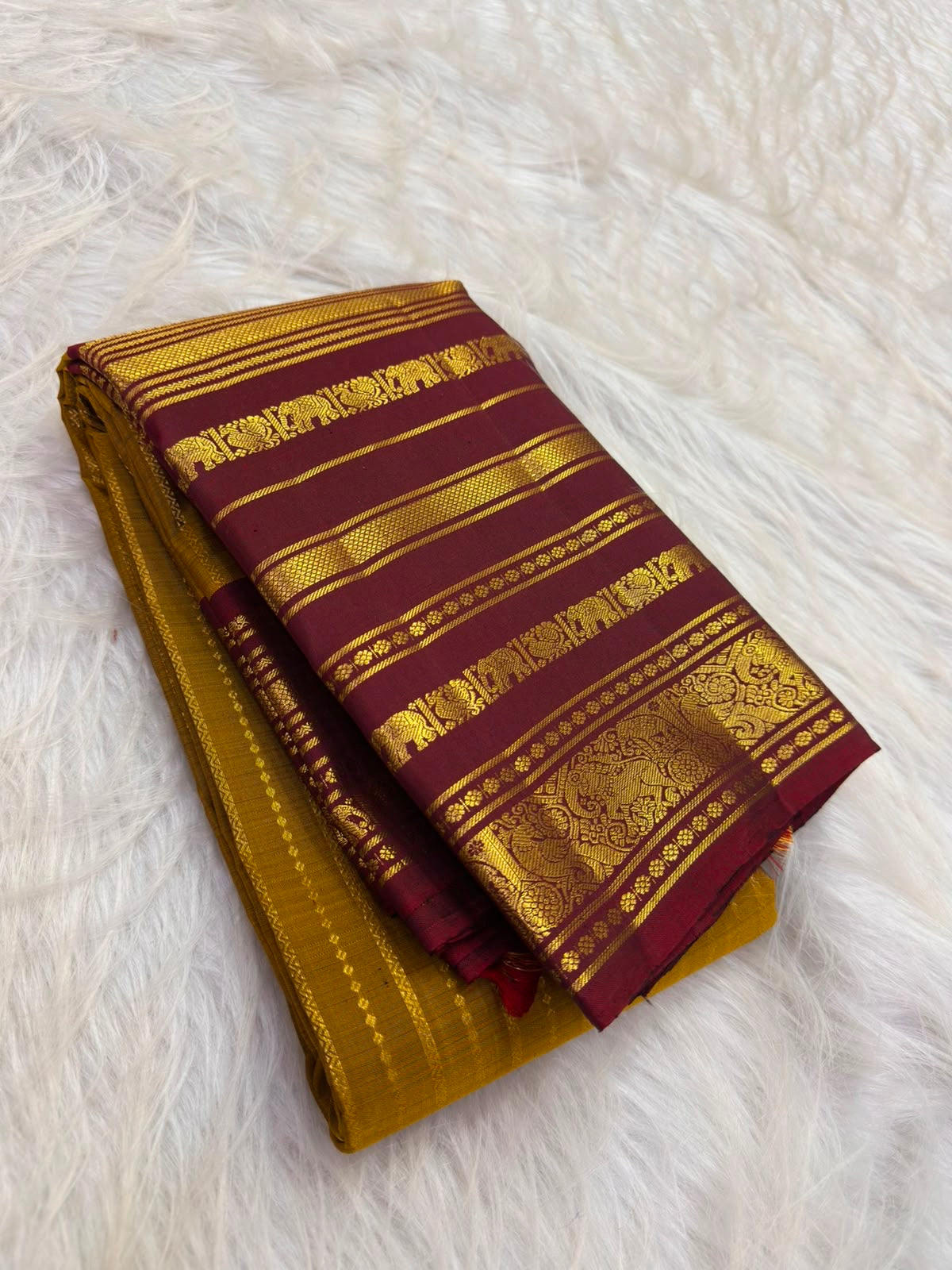 Gold zari border close-up showing fine horizontal bands, floral accents and repeated elephant motifs.