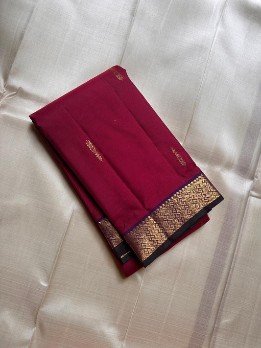 Folded deep maroon Pure Kanchipuram silk saree with small zari buttas and a gold zari woven border with dark edging.