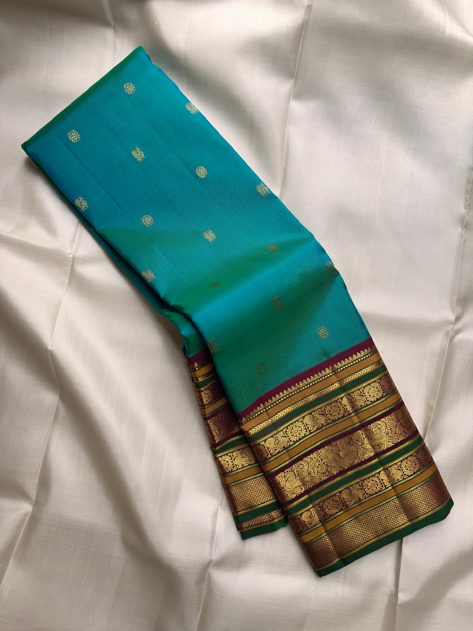 Deep maroon Kanchipuram Varisaipet pallu densely woven with gold zari ornamental columns and rich green accents.