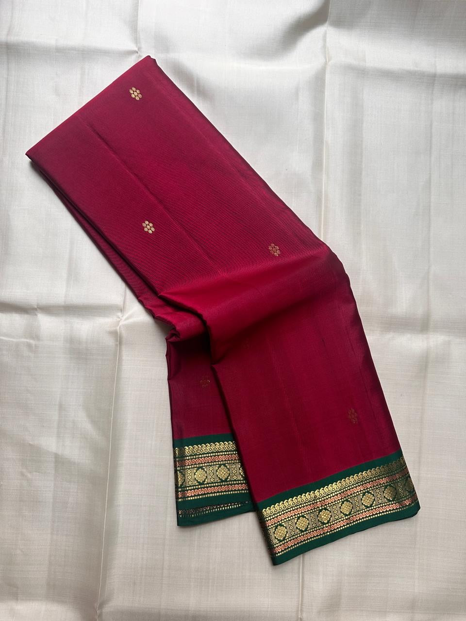 Pure Kanchipuram silk saree folded view showing deep pink body with small gold zari buttas and green contrast border
