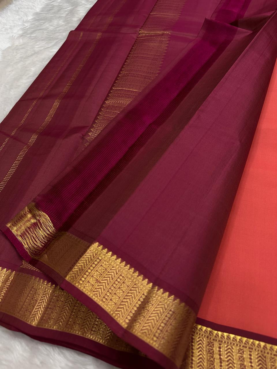 coral pink pure kanchipuram silk saree neatly folded showing narrow gold zari border