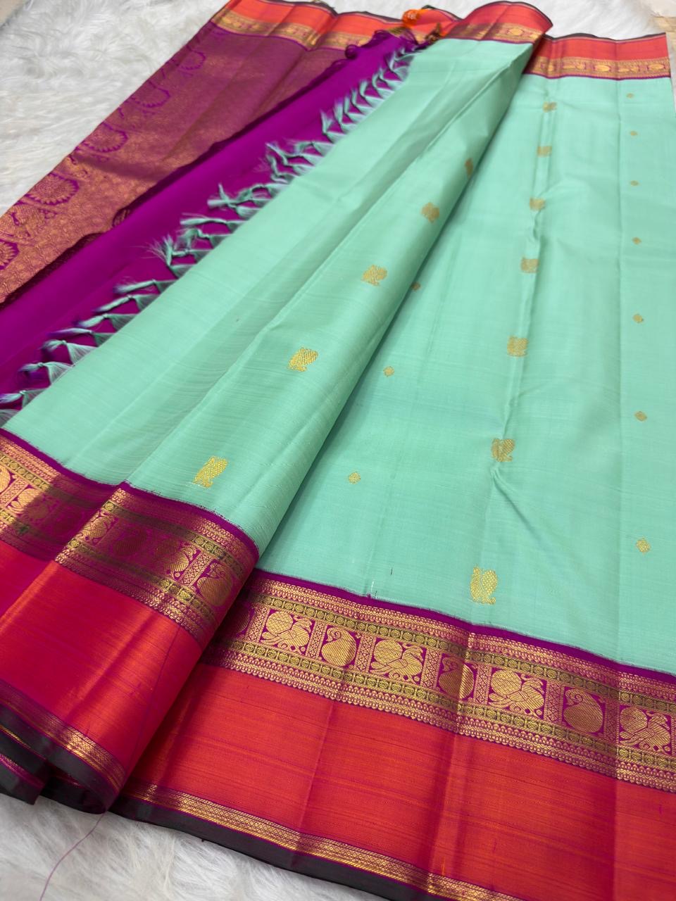 Close view of alternating Mayil and petite Kamalam gold-zari buttas across the mint silk body.