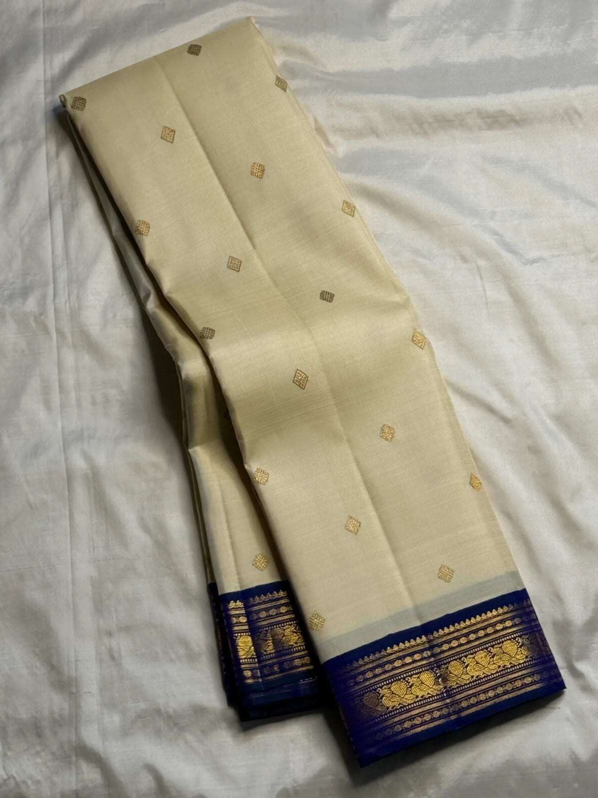 Close view of gold Mayil zari motifs woven across a deep blue-green Kanchipuram Korvai border.