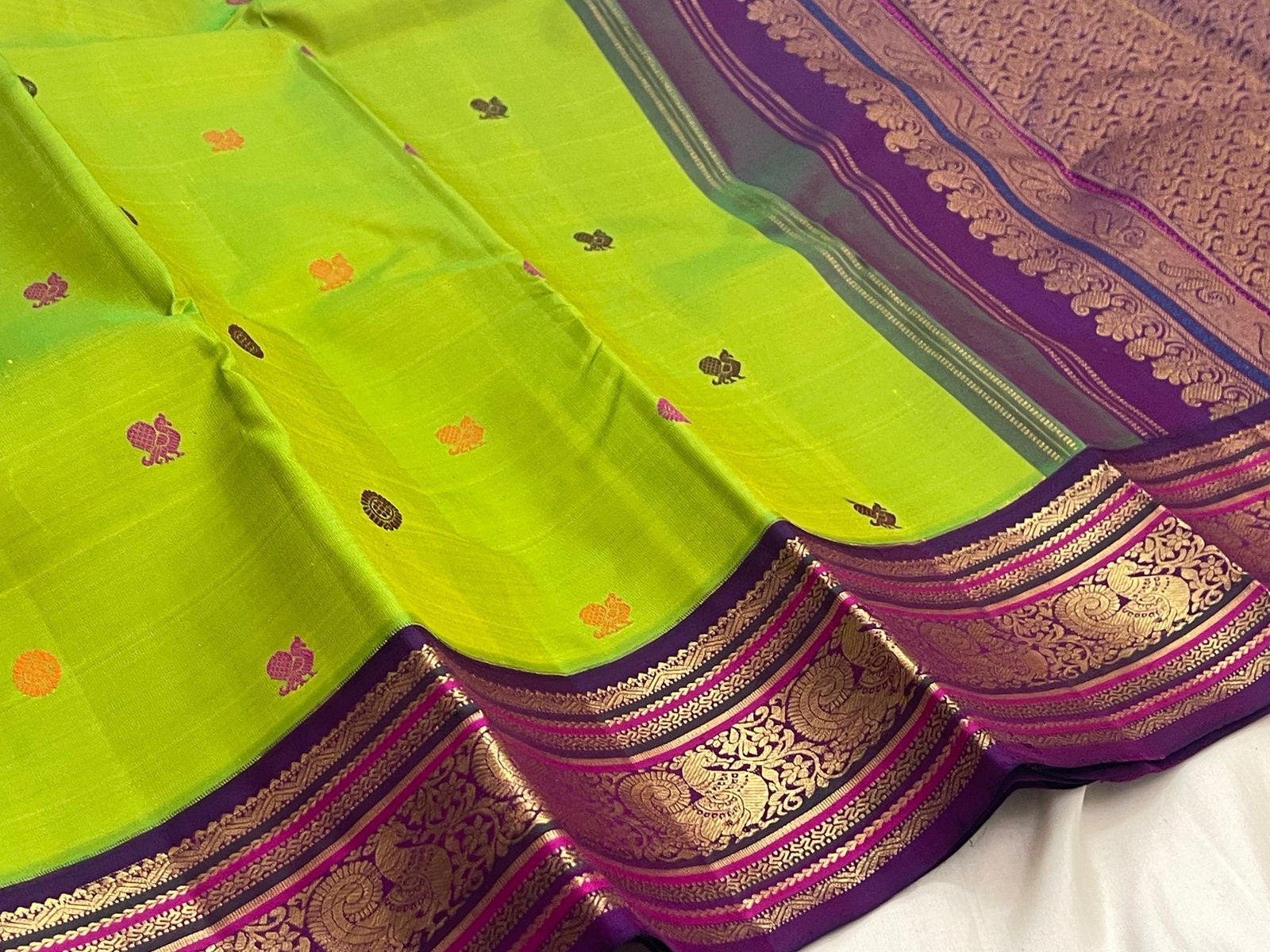 Full view of Parrot Green Kanchipuram Korvai saree showing multicoloured silk-thread buttas and dense Deep Purple gold zari pallu.