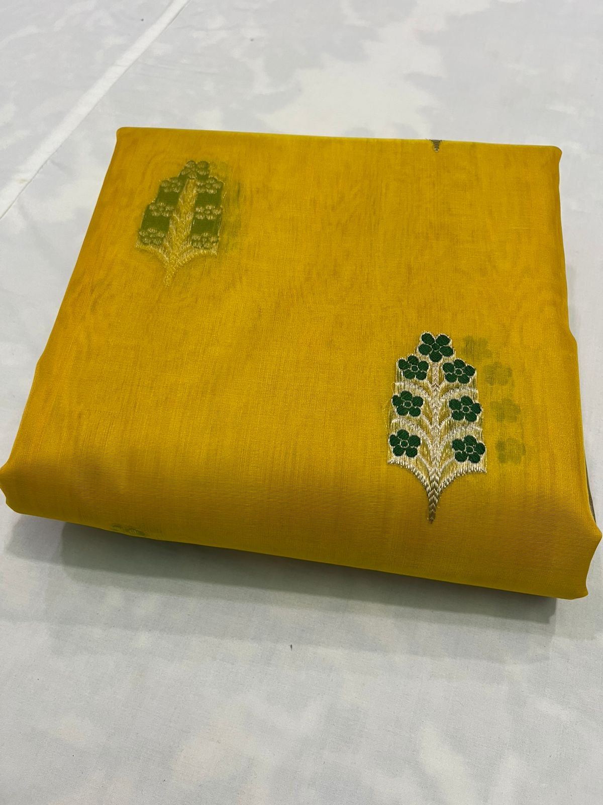 Yellow fabric with green floral embroidery on a white background