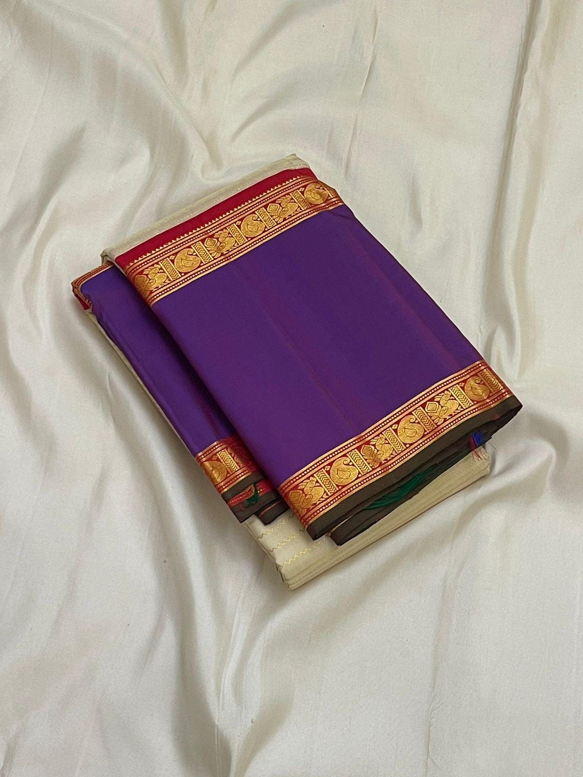 Folded pure Kanchipuram silk saree showing solid purple panel with red and gold zari woven border