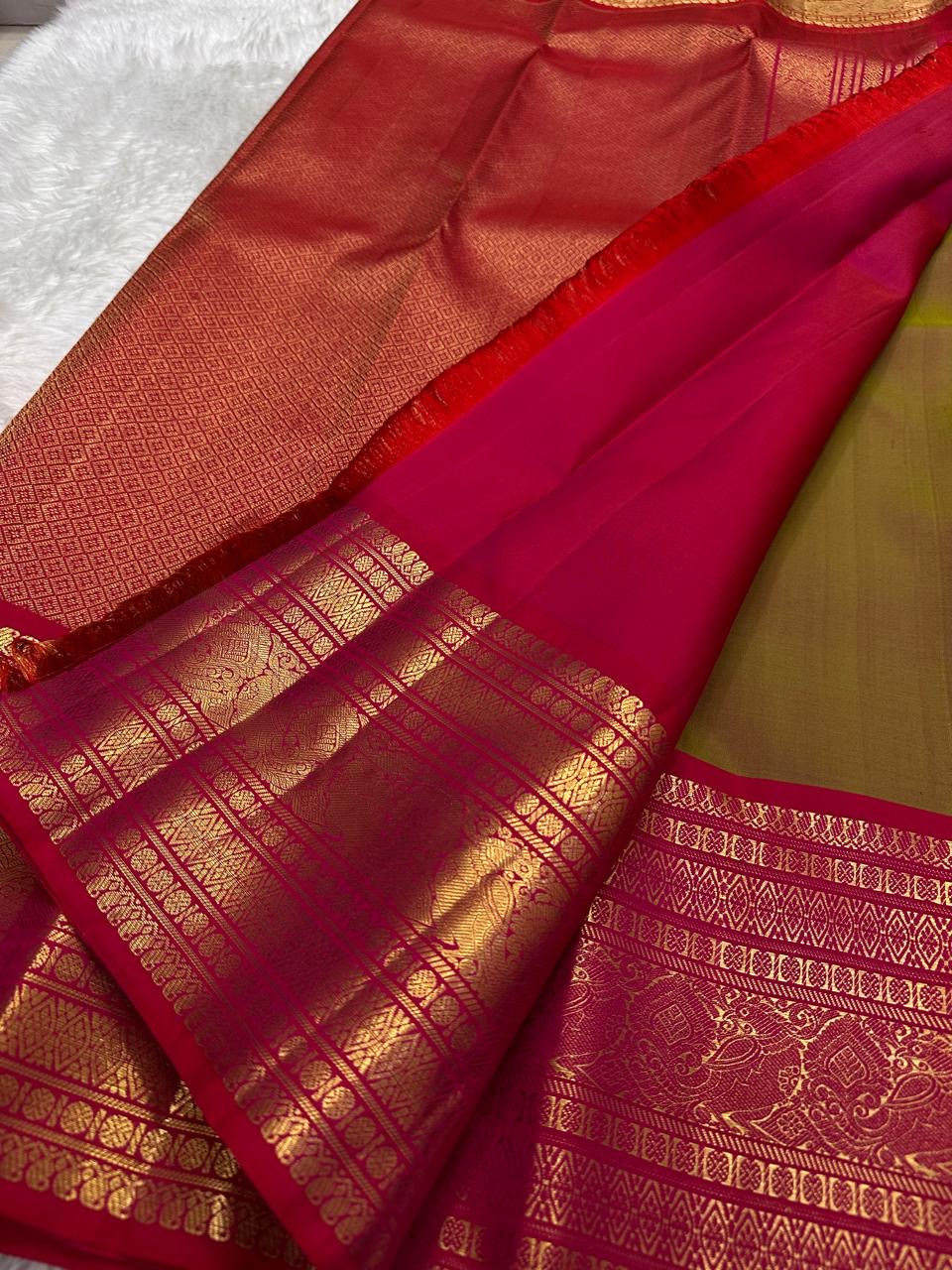 Unfolded olive-brown silk body with gold peacock buttas and a richly patterned ruby-pink border.
