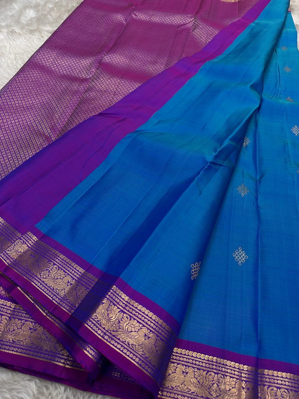 Pure Kanchipuram silk saree spread open with a teal blue body, zari buttas, and a contrasting purple pallu section.