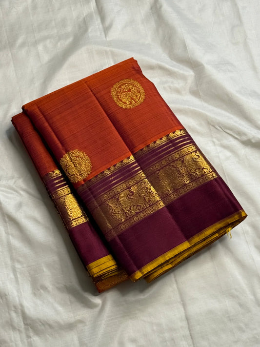 Folded rust orange Pure Kanchipuram silk saree with deep purple border and gold zari woven detailing